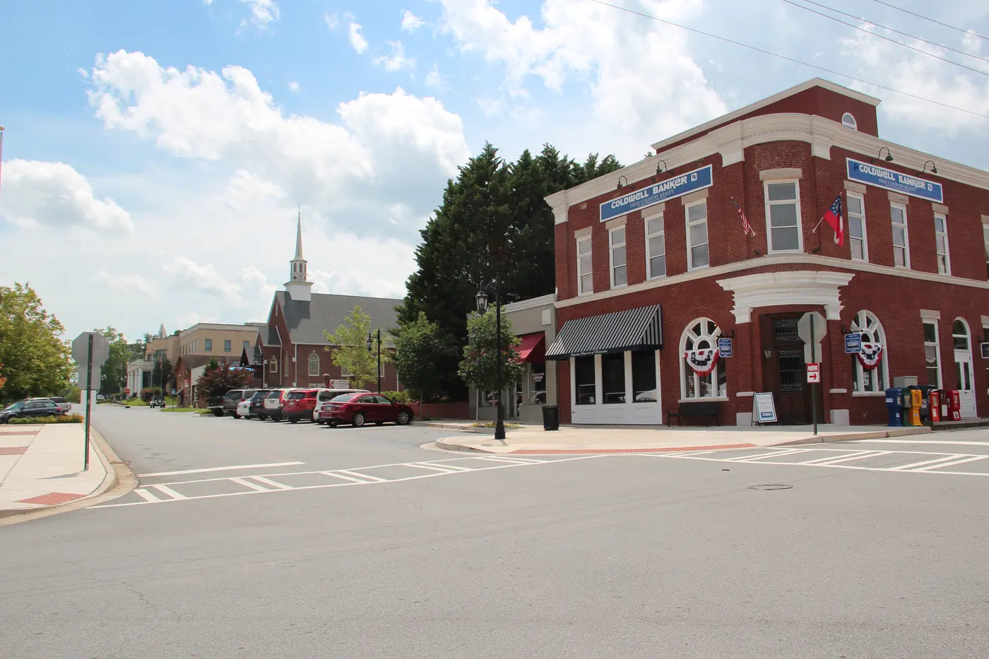 Brick commercial building at a street corner with a white church steeple down the road