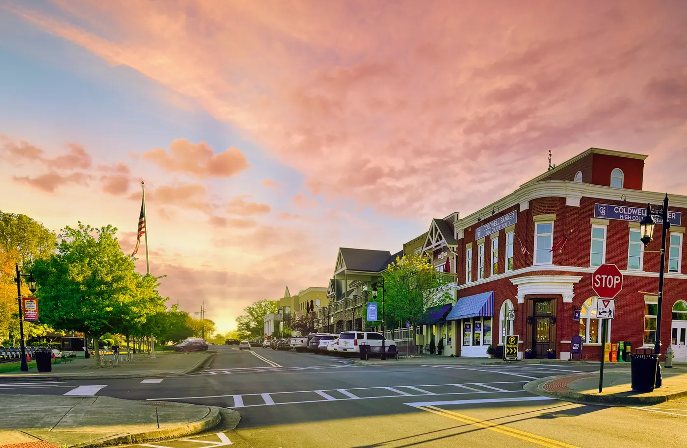 Red-brick corner building and storefronts on a quiet street at sunset under pink clouds