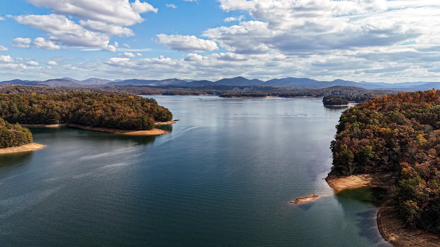 Elevated view of a lake channel between wooded points in fall color, with distant blue mountains