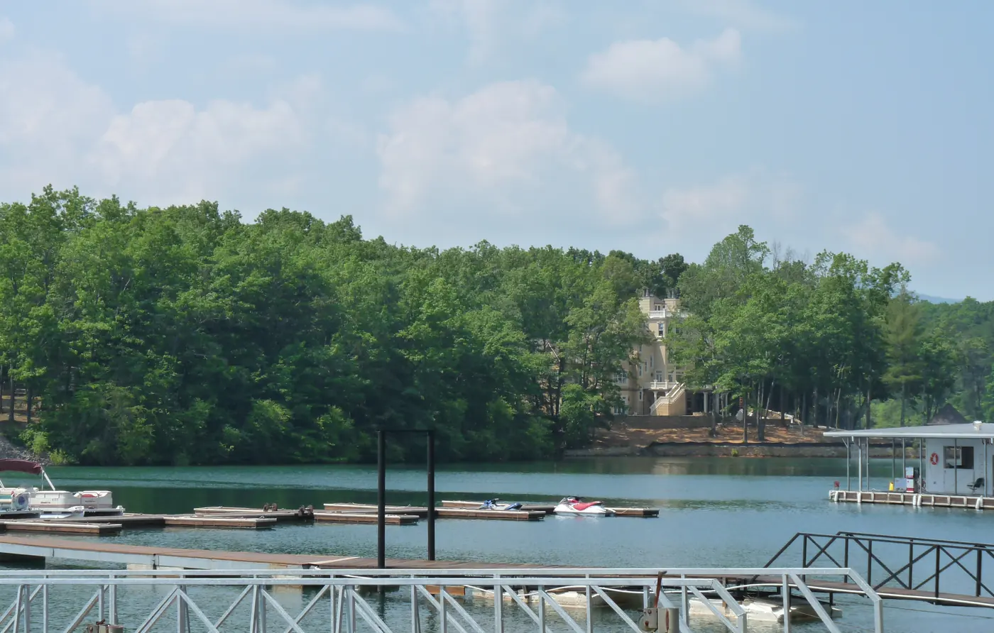 Boat docks and covered slips on a lake below a wooded hillside with a house among the trees