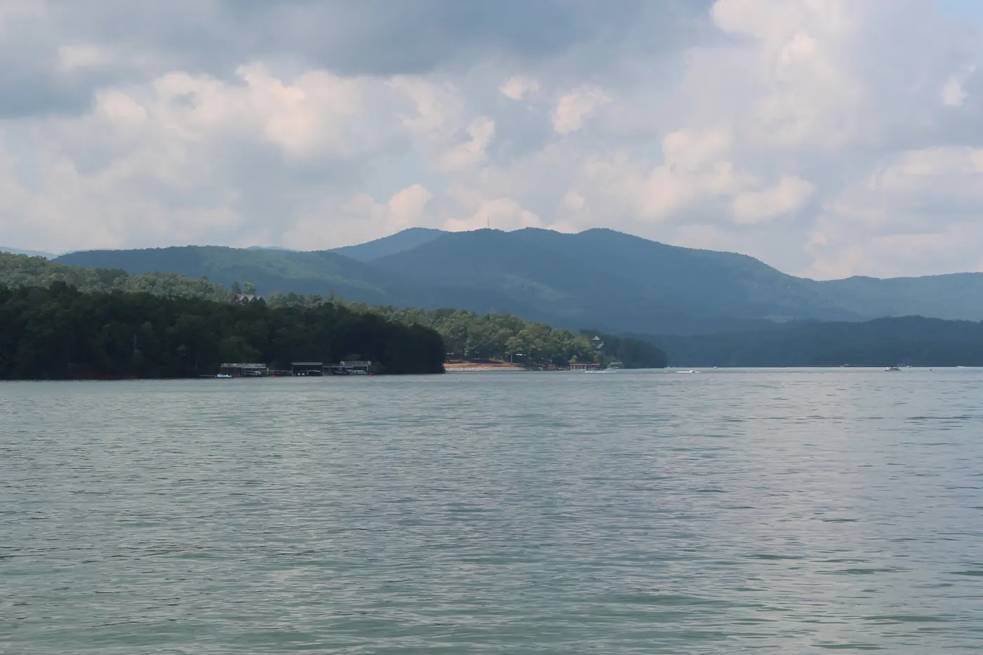 Open lake water with a wooded peninsula and a ridge of mountains beneath a cloudy sky