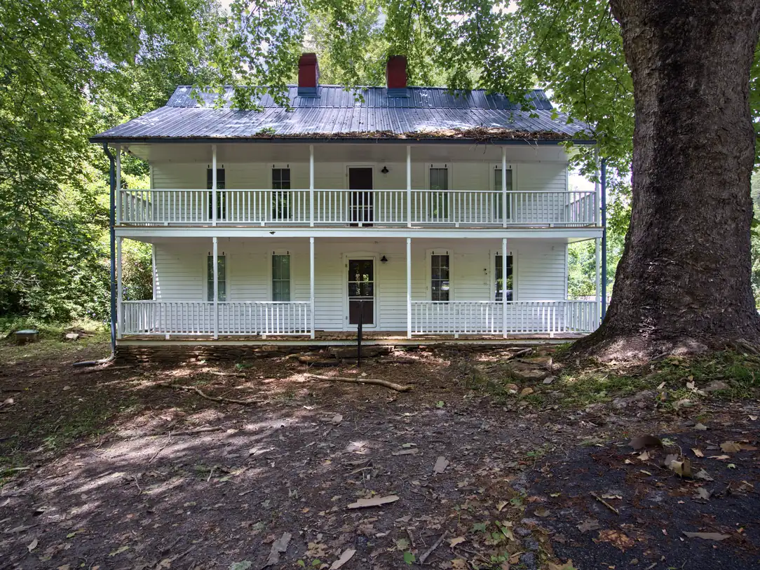Two-story white frame house with double porches beneath a large old tree