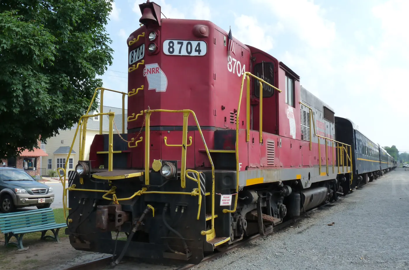 Red diesel locomotive numbered 8704 with passenger cars on a gravel rail yard