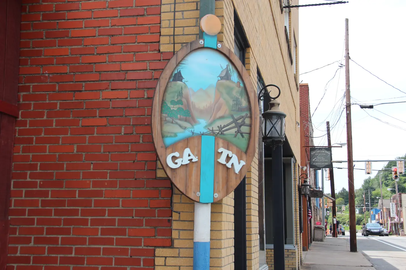 Painted oval sign marked GA and TN on a post beside brick storefronts along a sidewalk