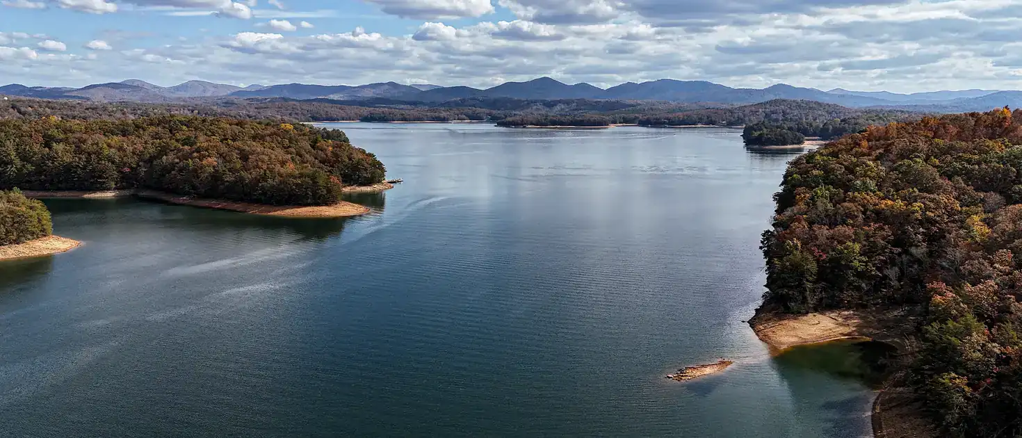 Lake Blue Ridge in autumn seen from above: calm water between wooded points in fall color, blue mountains beyond.